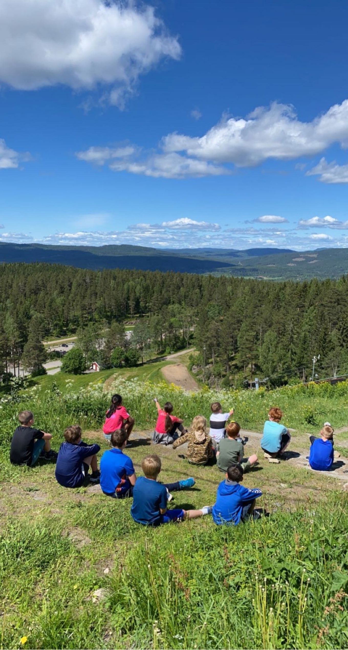 Elever som sitter på kulen på Linderudkollen hoppbakke og ser utover Lillomarka.